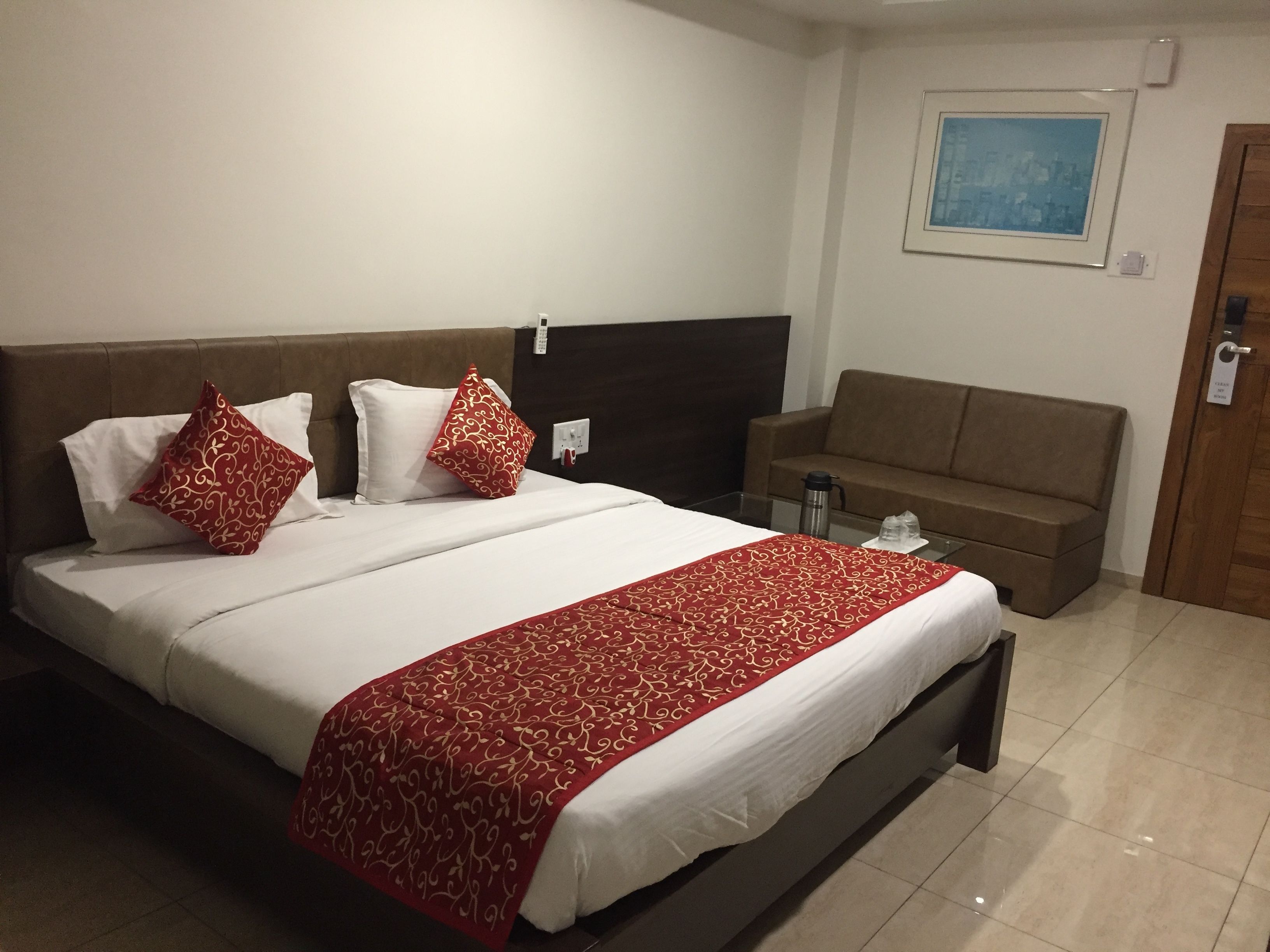 A hotel room with a large bed, a brown headboard, a brown sofa, and a framed picture on the wall.