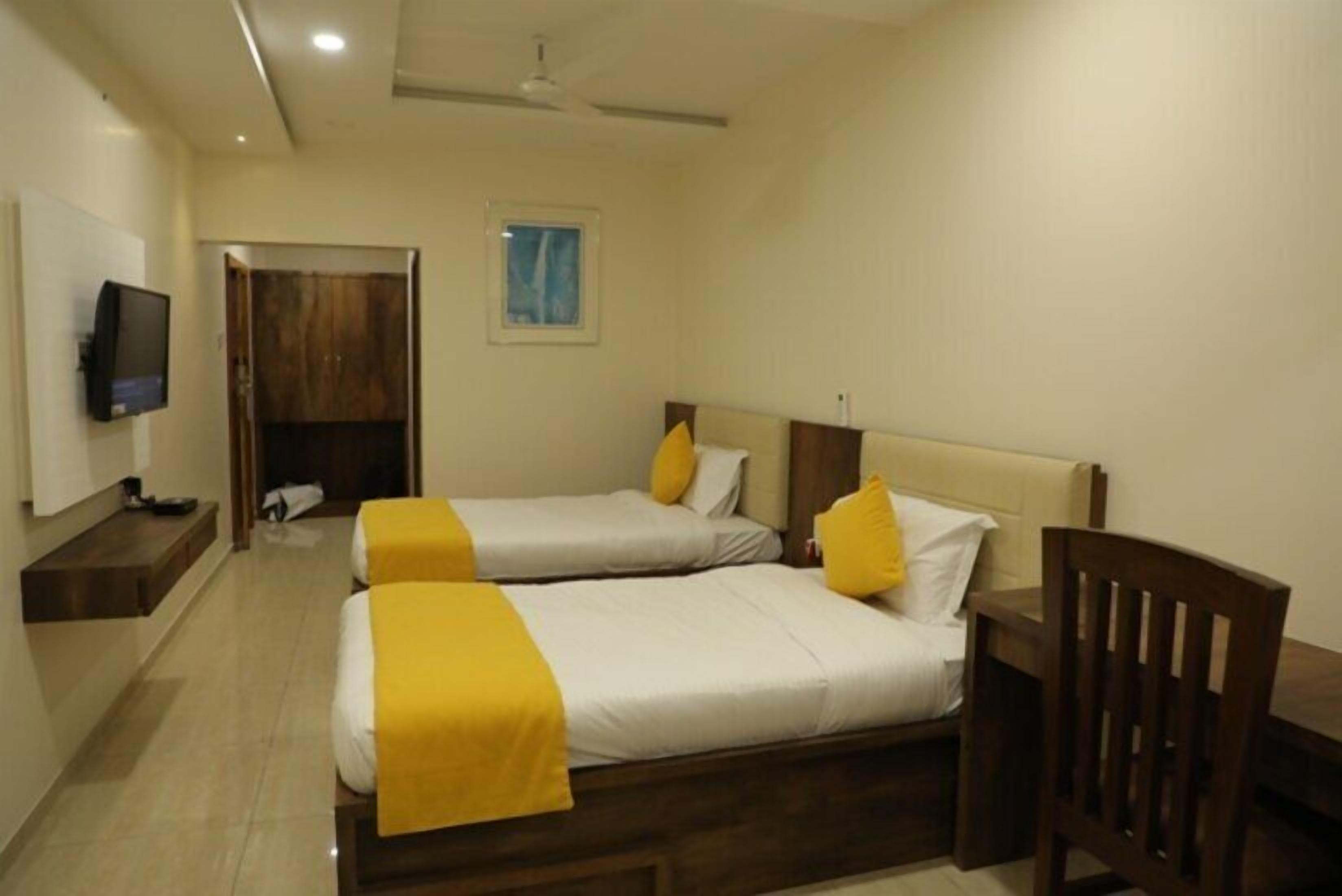Une chambre d’hôtel avec deux lits, un téléviseur, une chaise en bois et un ventilateur de plafond.