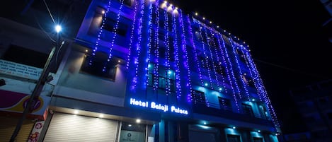 A building with the sign "Hotel Balaji Palace" and a series of lights on the facade.