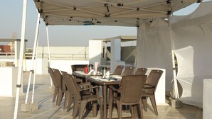 Un'area pranzo all'aperto coperta, con tavolo e sedie, circondata da tende bianche.
