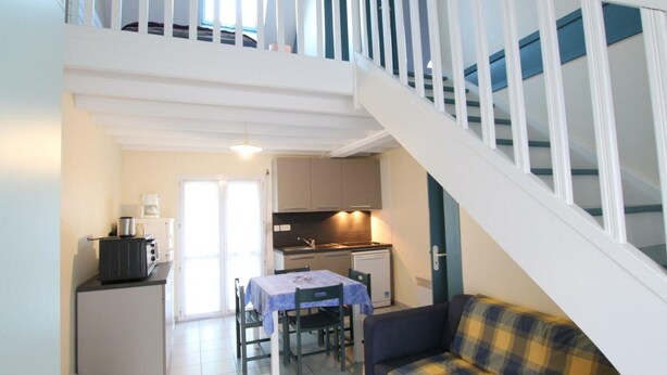 Un apartamento de dos pisos con una escalera, un comedor con mesa y sillas, una kitchenette y un sofá.
