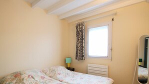 Un dormitorio con dos camas, una ventana con cortinas, una lámpara de noche, un radiador y un espejo de cuerpo entero.
