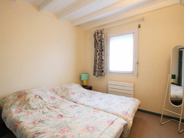 A bedroom with two beds, a window with curtains, a bedside lamp, a radiator, and a full-length mirror. - Cottage near beach with Wifi, garden and pets allowed (Siouville-Hague)
