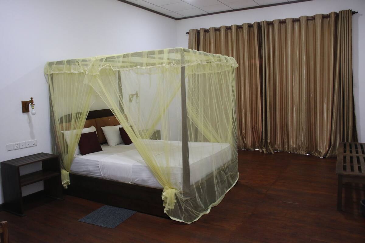 Una cama individual con mosquitero, una mesita de noche de madera, un escritorio y una silla.