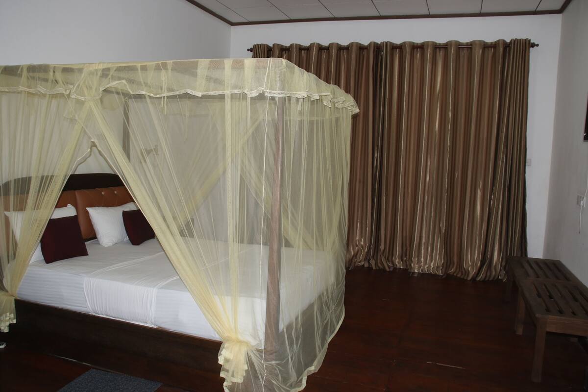Una habitación con una cama cubierta por una mosquitera, un banco de madera y cortinas.