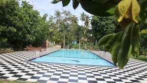A swimming pool with a checkered tile pattern, surrounded by greenery and trees.