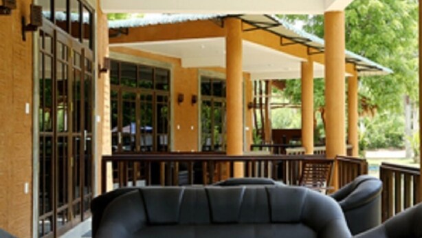 A covered outdoor seating area with a sofa and chairs, large windows, and a brick wall.