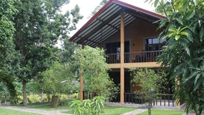 A two-story building with a covered balcony, surrounded by lush greenery and a paved walkway.