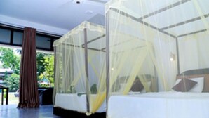 A modern hotel room with two beds covered by mosquito netting, a large window, and a view of greenery outside.