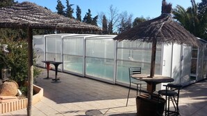 Un invernadero con estructura de vidrio, techo de paja y una piscina.