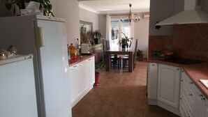 Una cocina con gabinetes blancos, una zona de comedor con mesa y sillas, y vistas al exterior a través de un ventanal.