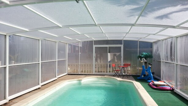 Una piscina cubierta con techo de vidrio, rodeada por una cerca y equipada con un sistema de filtración de agua.