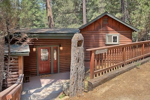 Cozy cabin with a wooden deck and stone wall, surrounded by trees.