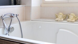 Ein Badezimmer mit Badewanne, einem Fenster und Dekoration, darunter getrocknete Pflanzen und Engel-Figurinen.
