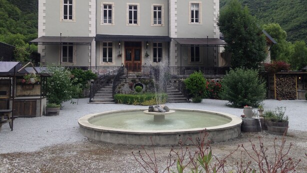 Ein großes, zweistöckiges Gebäude mit einer symmetrischen Fassade, einem zentralen Eingang mit einer Treppe und einem runden Brunnen im Innenhof.