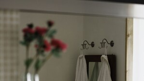 Ein Badezimmer mit einer Glastrennwand, einer Vase mit Blumen, einem Spiegel und zwei Handtüchern, die an Haken hängen.