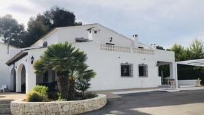 A white building with a stone circular planter, a covered patio, and a clear sky. - Villa 500m from the beach. Private pool.  (Teulada)