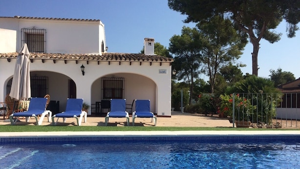 A pool area with blue lounge chairs and a white building with arches. - Villa 500m from the beach. Private pool.  (Teulada)