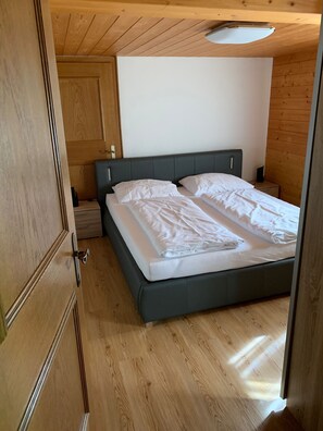 A bedroom with a bed, wooden flooring, and a door.