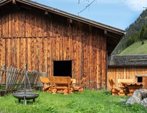 A rustic wooden barn with a large open door, a metal chair, and a fire pit in the foreground.