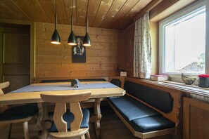 A wooden interior with a table and benches, a window with curtains, and a wall-mounted picture.