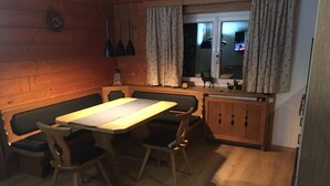 A wooden-paneled room with a table and chairs, a cabinet, and a window with curtains. - Quaint apartment in farmhouse (Schröcken)
