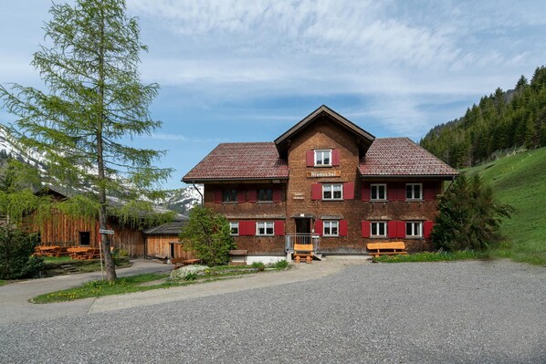 A two-story wooden building with a red-tiled roof, a sign reading 'Wiesenhof,' and a gravel driveway.