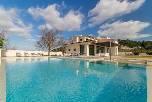 A modern pool area with lounge chairs and a building with large windows. - Dalt Son Morro, Villa 5StarsHome Mallorca (Santa Margalida)