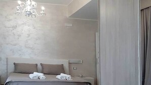 A modern bedroom with a large bed, a chandelier, and a wooden floor. - Hotel Aurora (Porto Cesareo)