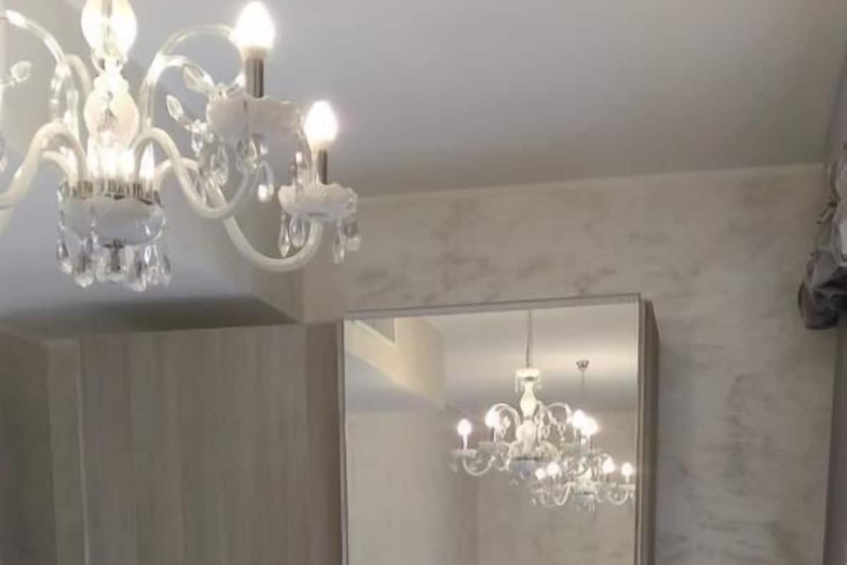 Un dormitorio con un espejo grande, una araña y una cama.