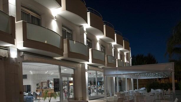 A hotel with multiple balconies, outdoor seating, and a covered patio area. - Hotel Aurora (Porto Cesareo)