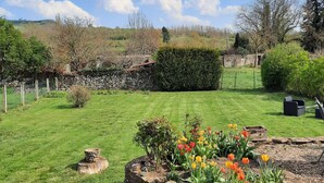 A well-maintained garden with a variety of plants and flowers, a stone wall, and a clear blue sky. - IN THE PEACEFUL HEART OF THE VINEYARD (Nolay)
