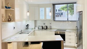 A modern kitchen with white cabinetry, a central island, stainless steel appliances, and a window with a view of a building. - A fantastic modern and spacious apartment right on Umhlanga main Beach . (Umhlanga)