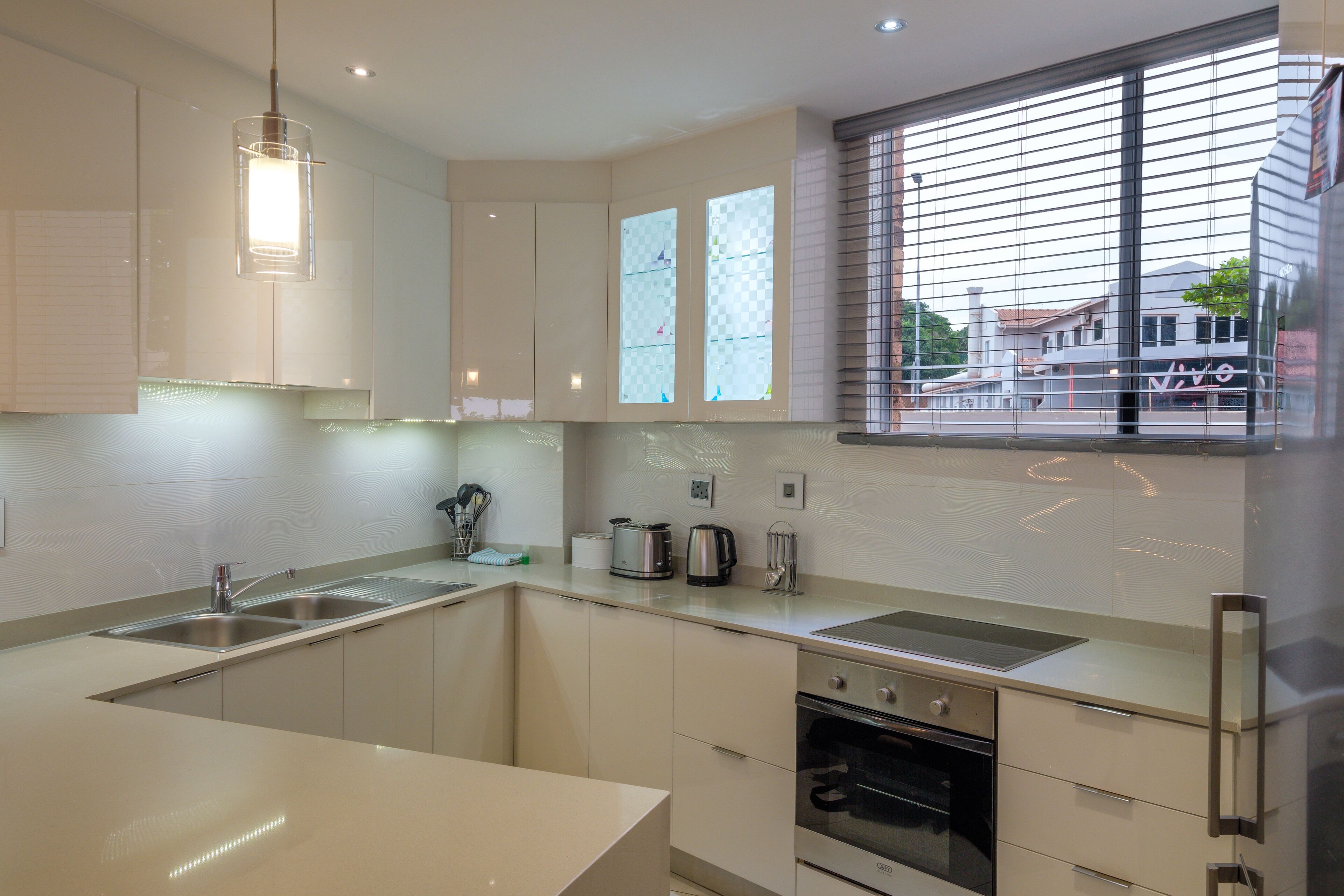 A modern kitchen with a large island, stainless steel appliances, and a window with blinds.