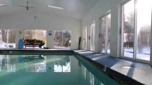 Ein Hallenbad mit großen Glaswänden, einem Deckenventilator und einer Sitzbank mit Büchern.