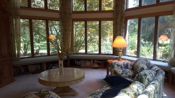 Ein gemütliches Zimmer mit großem Fenster, einem runden Tisch, einer Couch und einer Lampe.