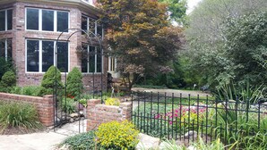 Ein Backsteinhaus mit Garten, einem Metallzaun und verschiedenen Pflanzen und Blumen.