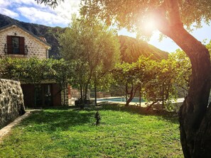 Ein Steinhaus mit einem Balkon, einem Schwimmbecken und einer Rasenfläche mit Bäumen.