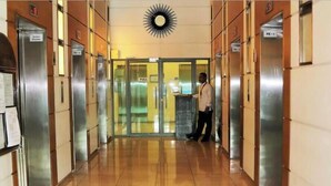 Hotelgang med elevatorer, et 'TRÆK' skilt og en solformet dekoration i loftet.