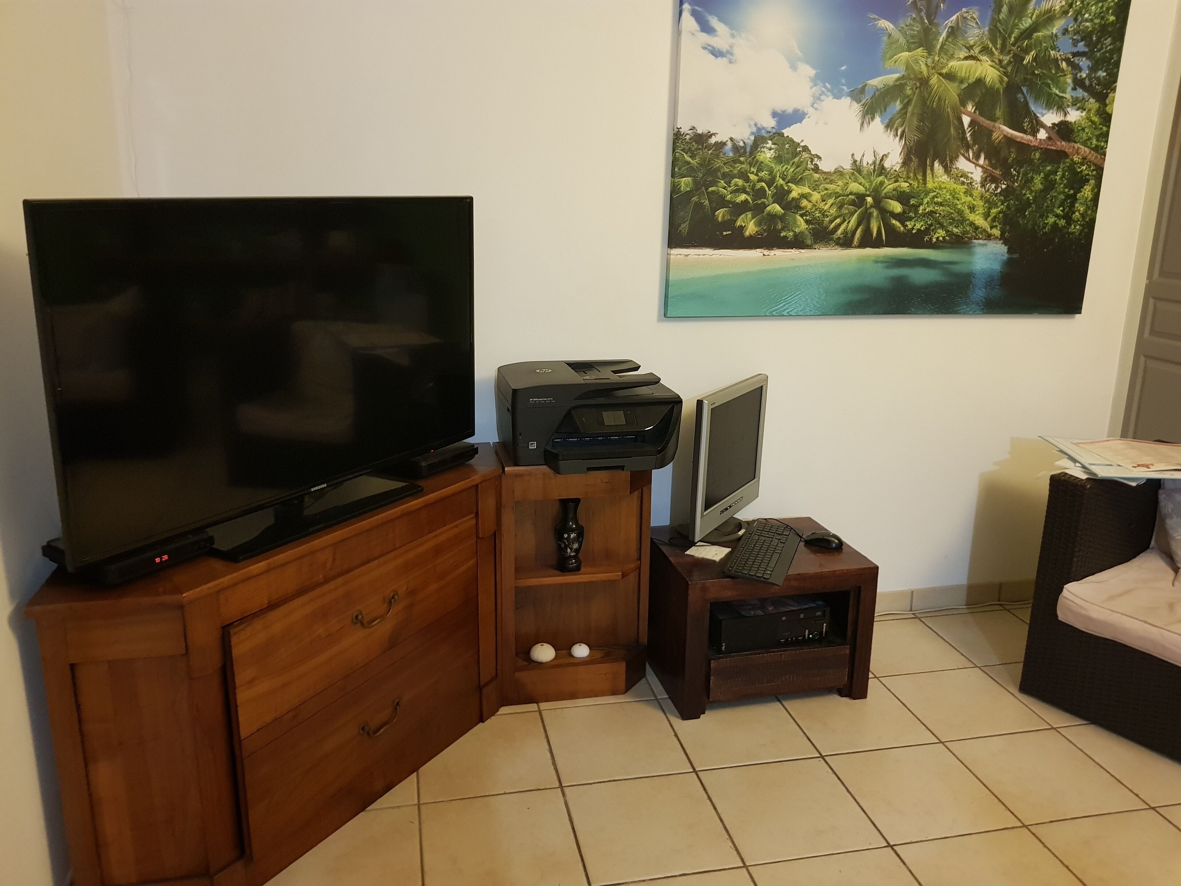 A living room with a flat-screen TV, a desktop computer, a printer, and a small table with a keyboard and mouse.