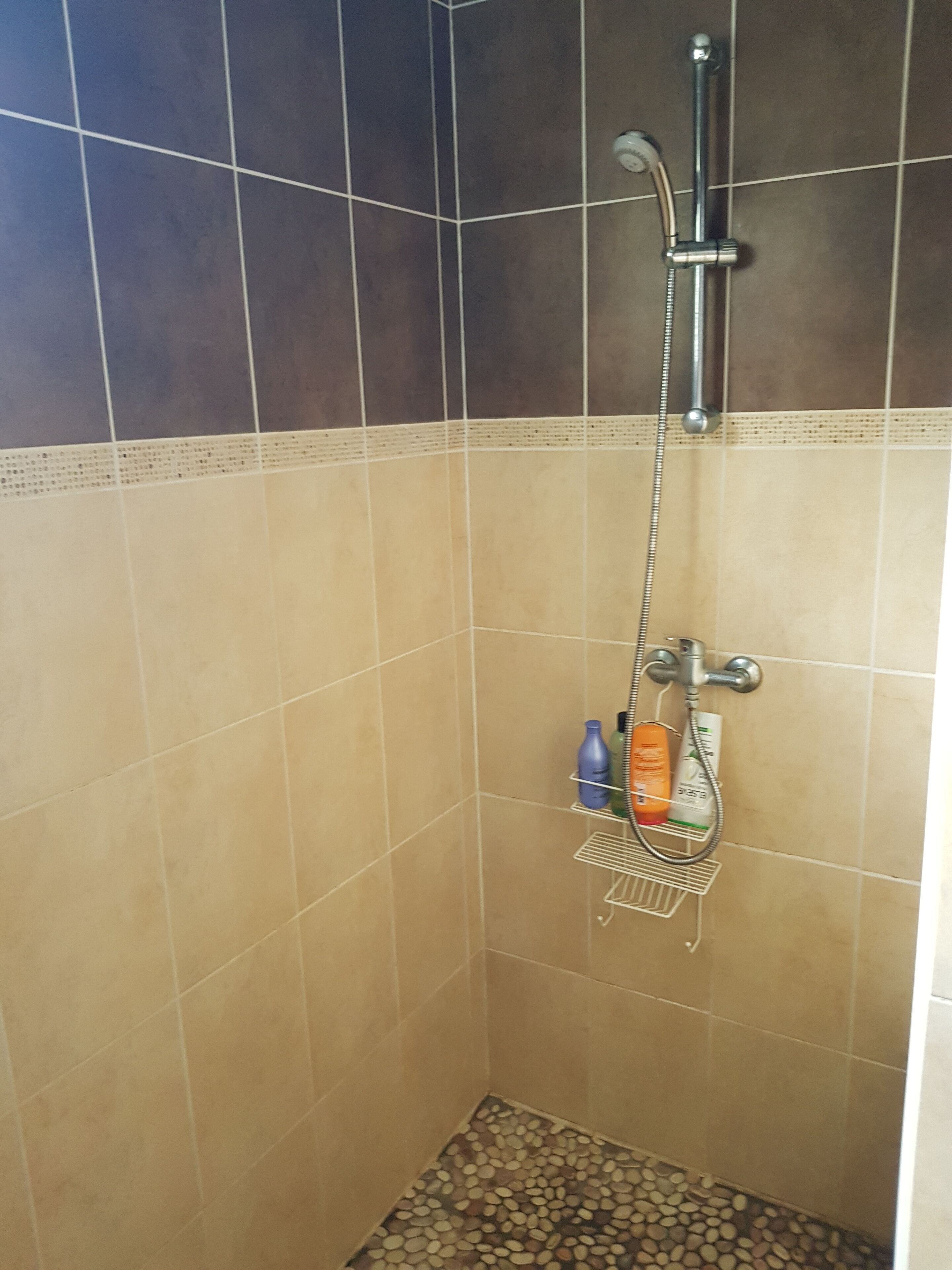 Una doccia con soffione a mano, rubinetto a parete e ripiano con articoli da toilette.