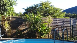 A rectangular swimming pool with metal ladders, surrounded by a wooden fence and various plants. - Villa with Caribbean Sea Small Pool (Les Trois-Îlets)
