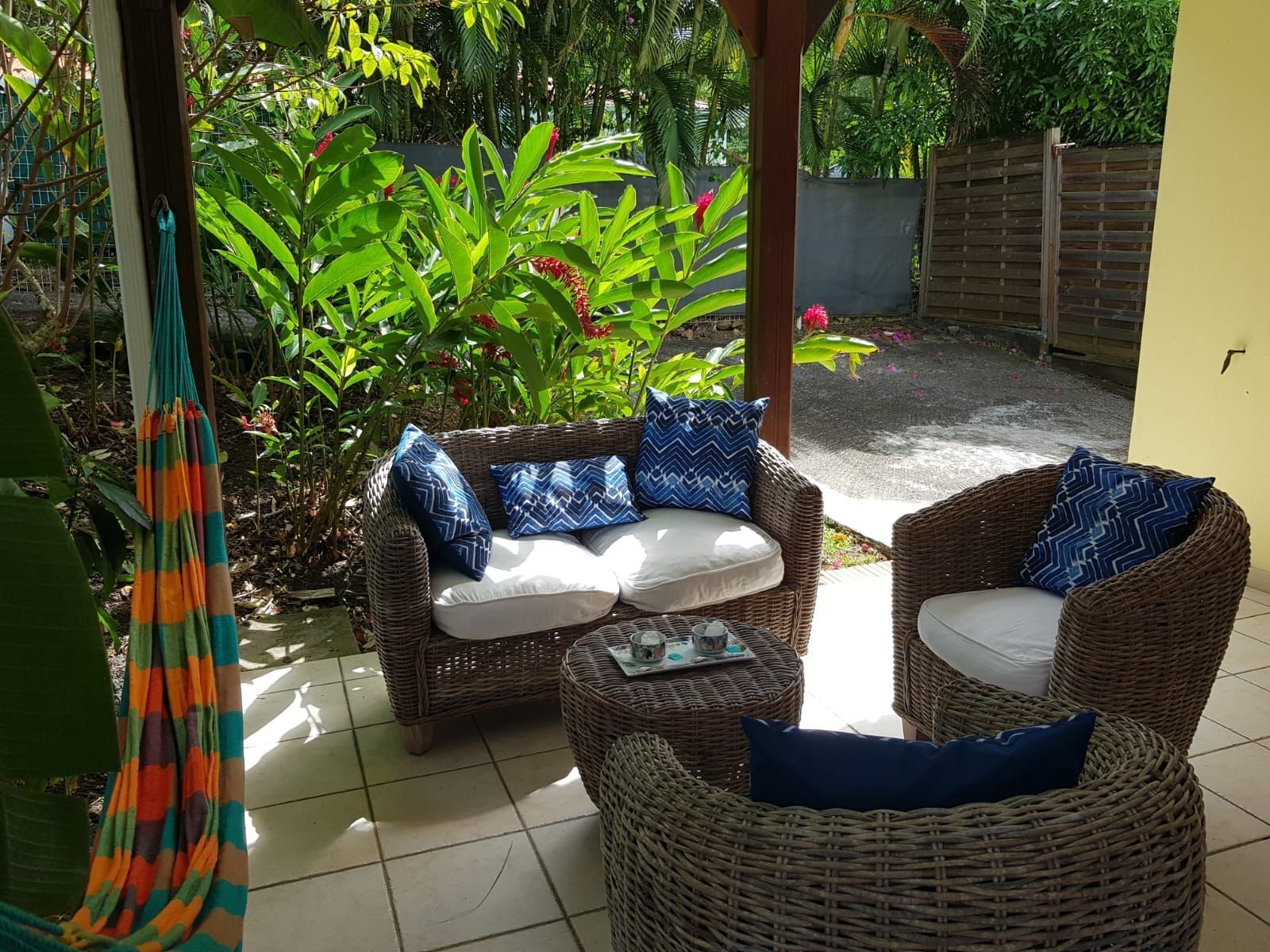 A wicker sofa and chair set with blue patterned cushions, a hanging hammock, and a tiled floor.