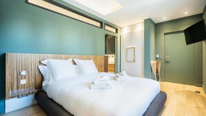 Camera d'albergo moderna con un ampio letto, una testiera in legno e un televisore a schermo piatto appeso al muro.