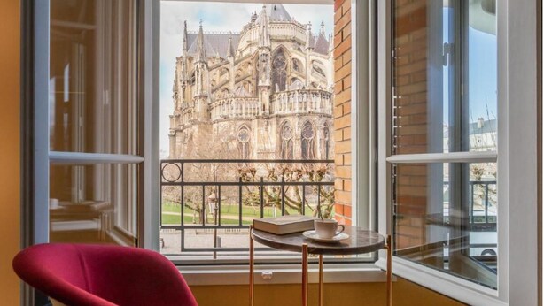 Una stanza con una sedia rossa, un tavolino con una tazza e vista su un'antica cattedrale attraverso una finestra.
