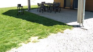 Un espace extérieur abrité avec une table et des chaises, une petite table avec une chaise, et un bâtiment avec un revêtement en bois et une porte.