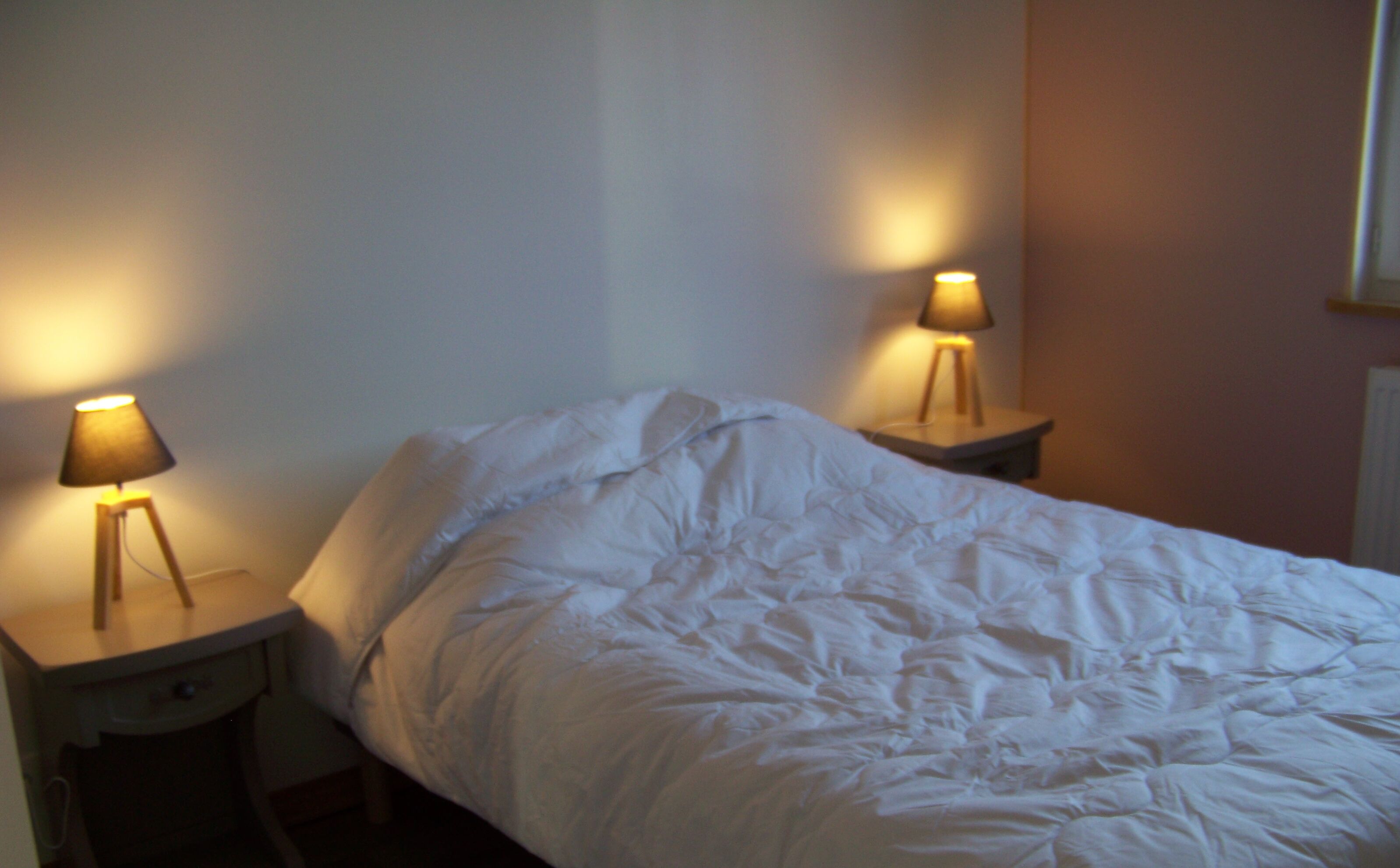 Una cama con ropa de cama blanca en una habitación con dos mesitas de noche, cada una con una lámpara.