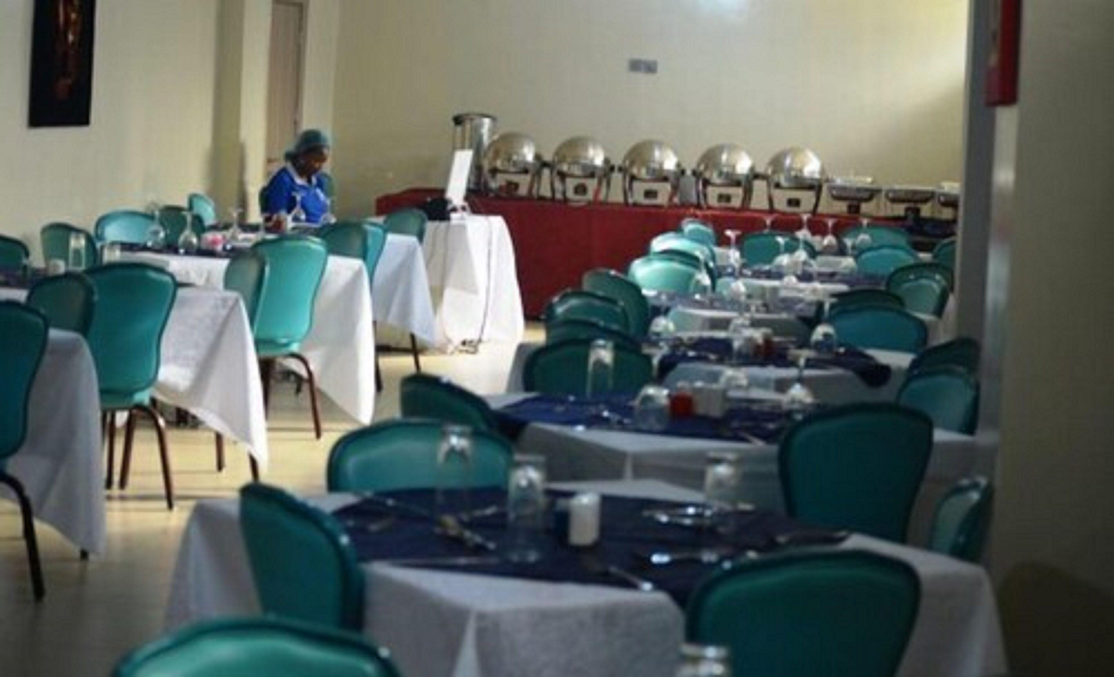 A conference room with rows of tables and chairs, a podium, and a person standing at the front.