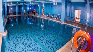 Una piscina interior con suelo y paredes de baldosas azules, un flotador y una persona al fondo.