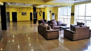 Un vestíbulo amplio con piso pulido, paredes amarillas y una zona de estar con sofás y una mesa de centro.